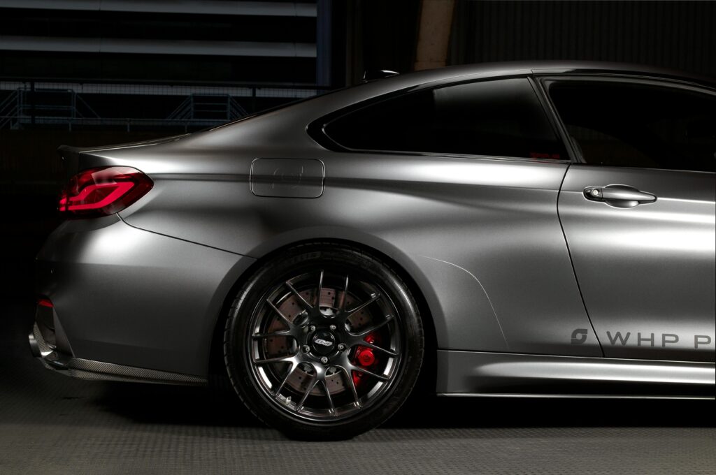 Close-up of a silver luxury car with focus on the wheel and tail light at night.